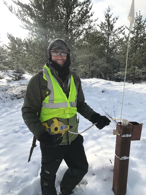 Forrest Gilfoy measuring aquifer water levels in a forested setting
